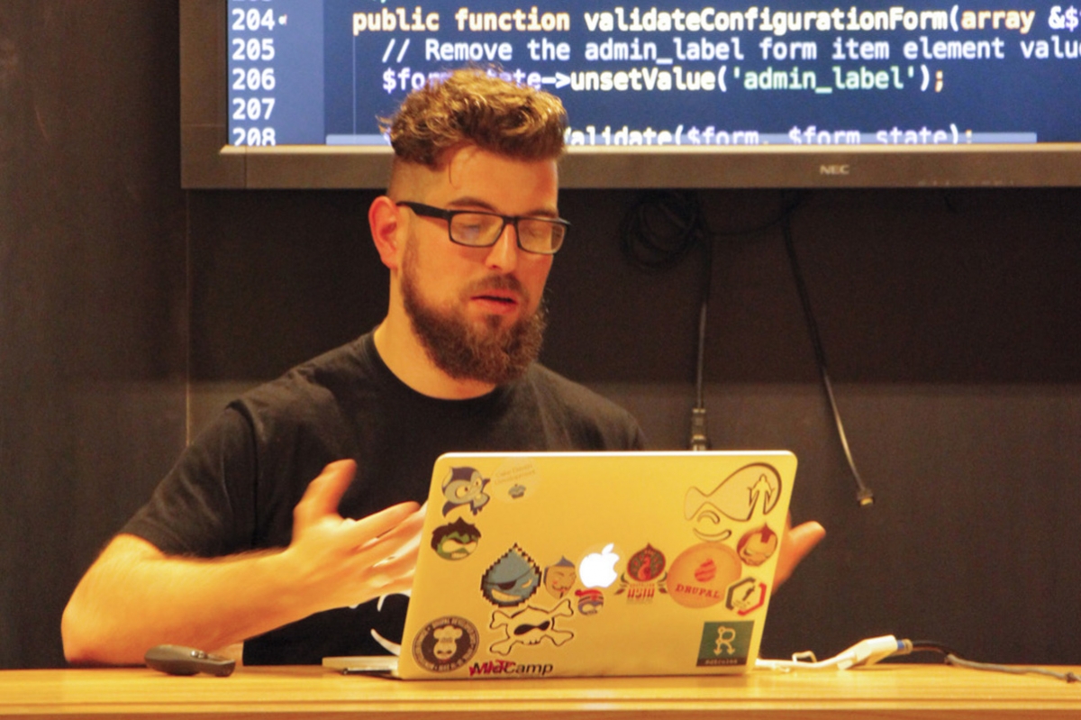 Bart presenteert van achter zijn laptop, code op het beamer scherm in de achtergrond